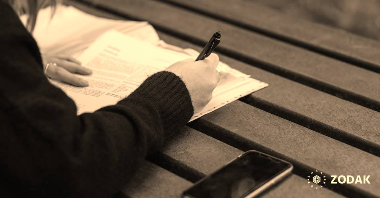 From above of crop anonymous female writing with pen in documents on wooden table in park