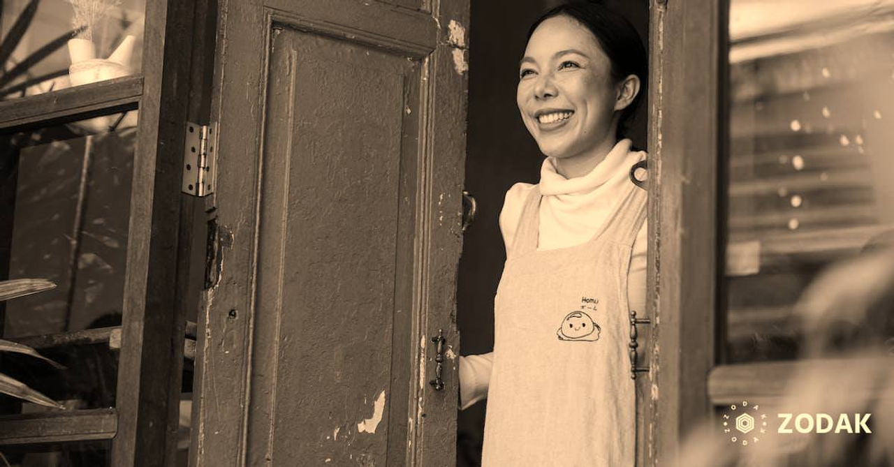 Happy ethnic coffee shop owner standing at entrance door