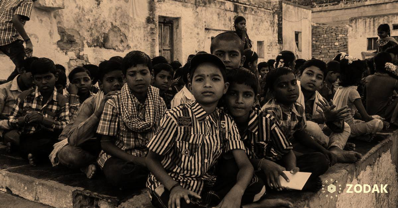 Ethnic barefoot kids in casual clothes sitting on stone floor while studying in local school and looking at camera