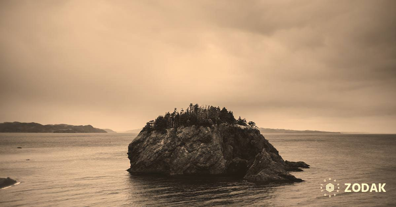 Amazing scenery of rocky uninhabited island in rippling sea located in Chance Cove coastal town against cloudy gray sky