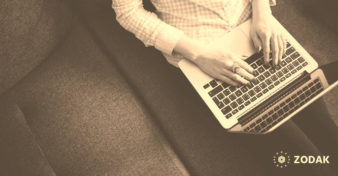 Person Sitting on Gray Sofa While Using Macbook