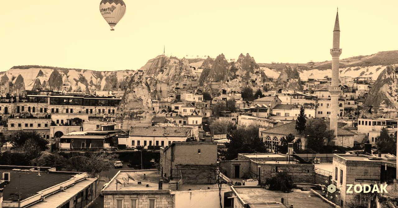 Colorful air balloon flying above shabby buildings and tall tower in famous national park Goreme in Turkey against cloudless sky