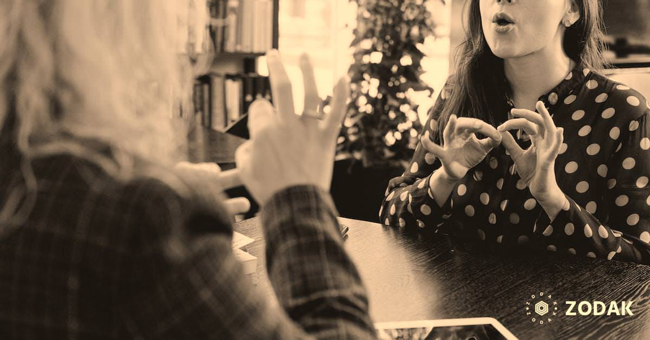 Young female friends communicating using sign language in library