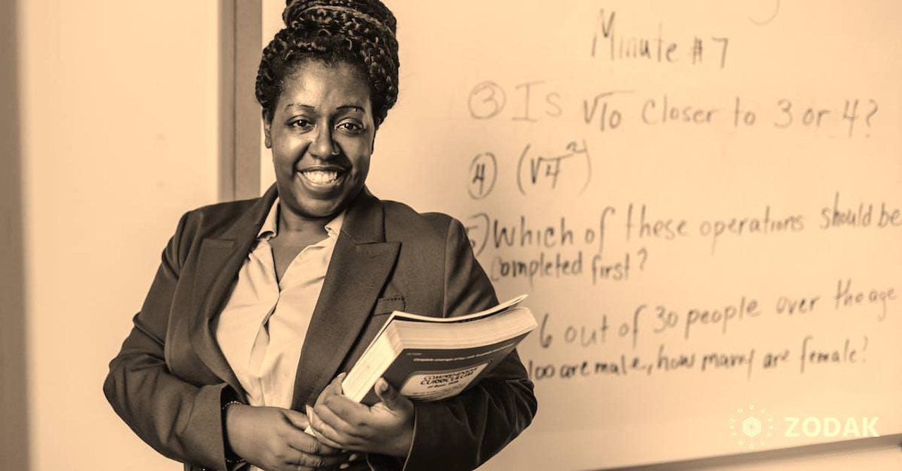 Cheerful black female teacher with workbooks standing near whiteboard