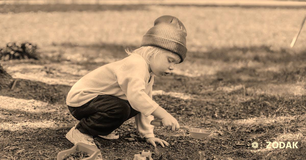 Side view of little boy in casual clothes and brown hat playing with plastic toys in backyard