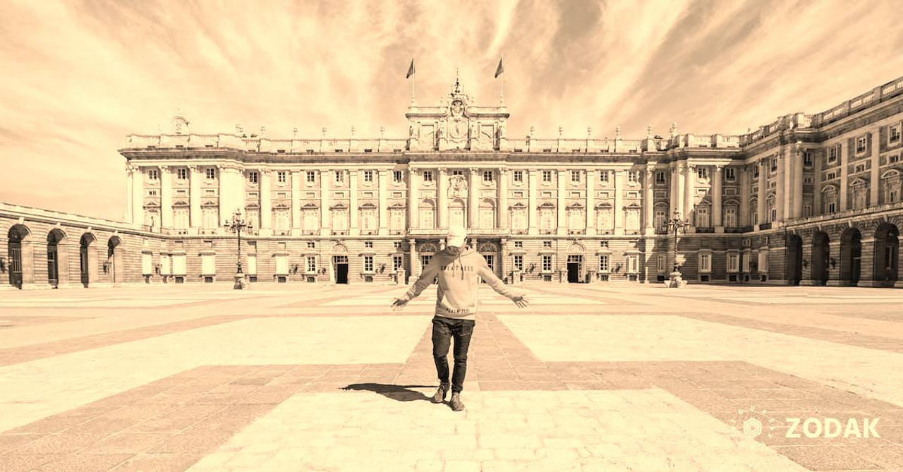 Full body of unrecognizable male traveler in casual clothes and cap standing on empty square near Royal Palace of Madrid during holiday in Spain