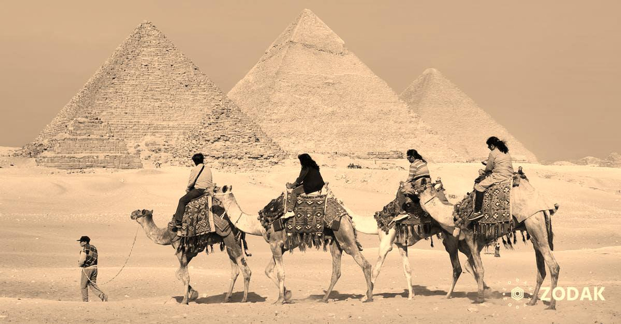 Four People Riding on Camels Across the Pyramids