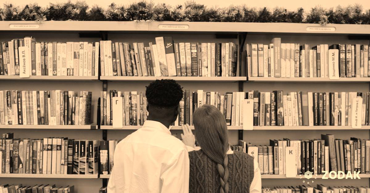 A Couple Standing by the Book on Shelves 