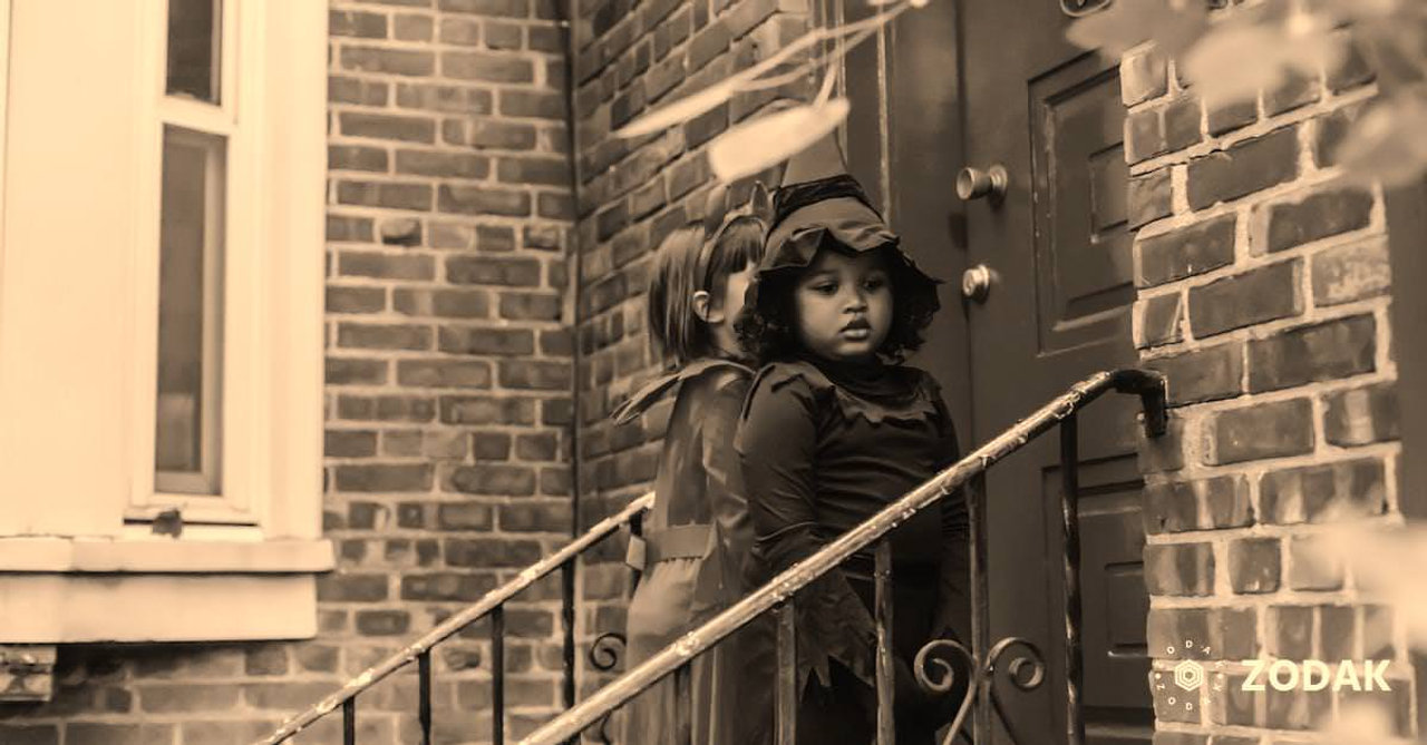 Multiethnic kids dressed for Halloween celebrations standing near front door of red brick house playing trick or treat custom