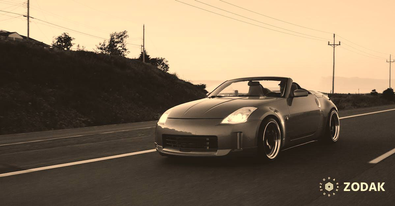 Luxury automobile riding on asphalt road with marking lines near rough slope covered with grass and trees