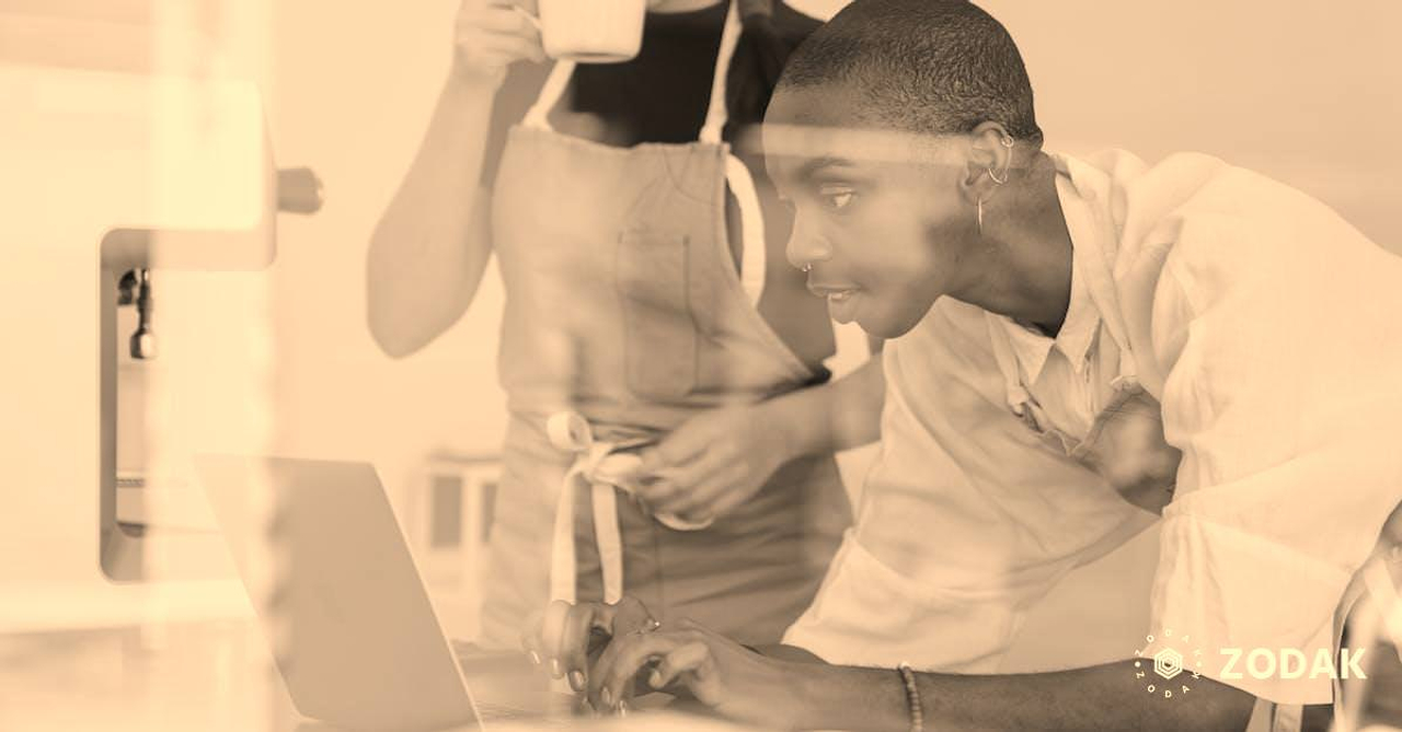 Black female barista together with colleague using laptop at work